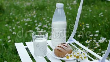 在洋甘菊草坪的中间，白色的椅子上有一瓶牛奶，还有一杯牛奶和面包。 附近